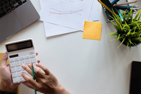Top view hand of accountant using calculator on workplace with copy space, calculator and plant potted on white desk background, Accounting workplace conceptの写真素材