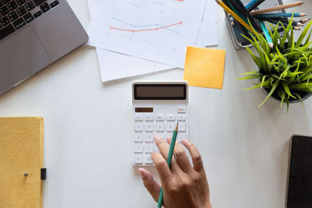 Top view hand of accountant using calculator on workplace with copy space, calculator and plant potted on white desk background, Accounting workplace conceptの写真素材