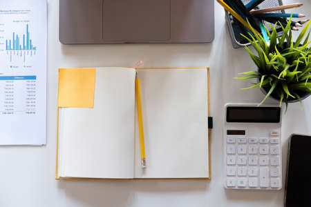 Top view open notebook, pencil, calculator and plant potted on white desk background, Accounting workplace conceptの写真素材