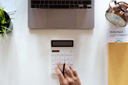Top view hand of accountant using calculator on workplace with copy space, calculator and plant potted on white desk background, Accounting workplace conceptの写真素材