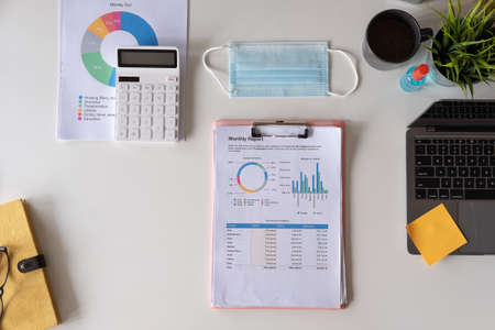 medical face mask and hand sanitizer on business financial work place. Flat lay with laptop computer and white workspace background with copy space. Top viewの写真素材