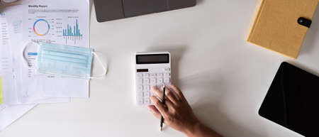 Top view hand of accountant using calculator on workplace, calculator and plant potted on white desk background, Accounting workplace conceptの写真素材