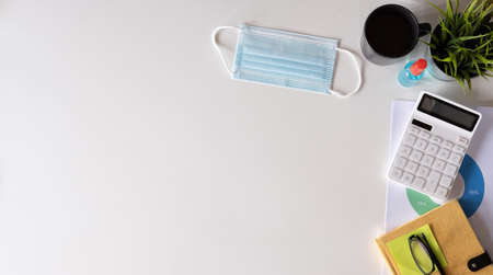 White office desk table with surgical face mask and sanitizer bottle or alcohol gel with calculator isolated on white background, work from home and covid-19 concept and new normal.の写真素材