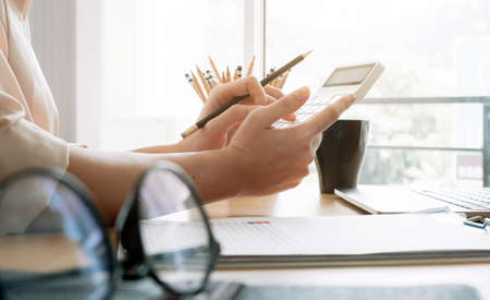 Close up of businesswoman or accountant hand holding pencil working on calculator to calculate financial data report, accountancy document and laptop computer at office, business concept.の写真素材