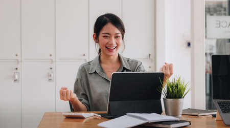 Portrait of an excited young asian girl using laptop computer and celebrating success for online learning or working at homeの写真素材