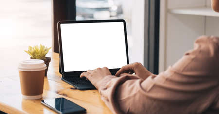 Cropped shot of young professional businesswoman typing on blank screen tablet and office supplies in simple workspace.の写真素材