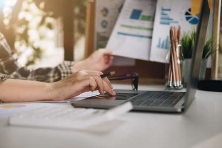 Close up of businessman or accountant hand holding pen working on laptop for business data,...