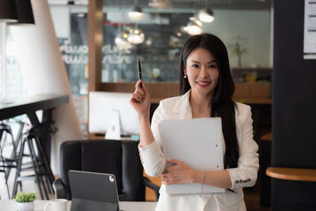 Smiling asian business woman looking at camera and working in her officeの写真素材