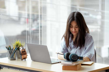 Online education. Asian girl with headphones makes an online lesson using a computer video call to a virtual teacher at homeの写真素材