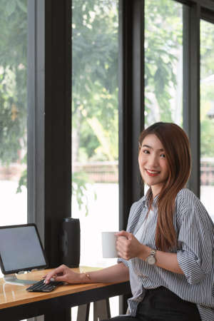 Image of a charming Asian woman working at a coffee shop cafe. Female freelance using digital tabletの写真素材