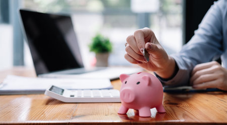 Close up hand of woman putting money coin into pink piggy bank for saving money wealth and financial conceptの写真素材