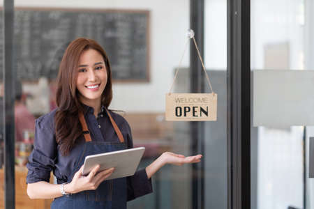 Portrait of a smiling Asian entrepreneur standing behind her cafe counter with open sign board
