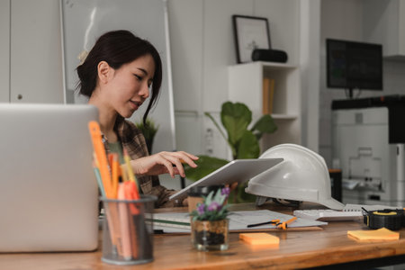 Woman architect designer structural engineer working office looking tablet discussing building plan design project. Architect working on digital tablet and laptop computerの写真素材