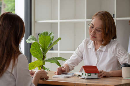 Real estate broker agent being analysis and making the decision a home estate loan to customer, She using calculator to presentation detail and waiting for her reply to finishの写真素材