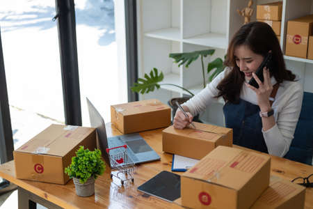Starting Small business entrepreneur SME freelance,Portrait young woman working at home office, BOX,smartphone,laptop, online, marketing, packaging, delivery, SME, e-commerce concept.の写真素材
