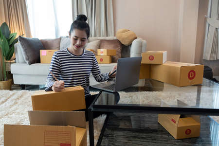 Young woman small business owner online shopping at home. confirm orders from customers with mobile...