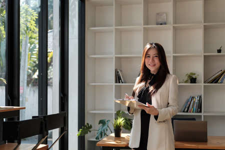 Portrait of business asian woman happy smile holding check list on clipboard and pen at modern offliceの写真素材