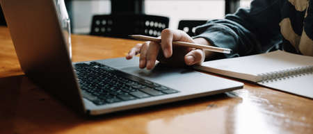 Cropped photo of asian woman using laptop and writing making list taking notes in notepad working or learning on laptop indoors- educational course or training, seminar, education online conceptの写真素材