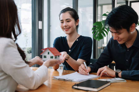 Real estate agent offer hand for customer sign agreement contract signature for buy or sell house. Happy asian couple signing a contract together at office. Real estate contact agreement conceptの写真素材
