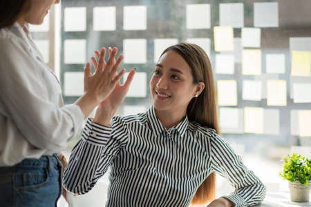 Two asian woman colleagues give each other high five, Successful business team working together...