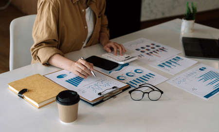 businesswoman or accountant hand holding pen working on calculator to calculate business data, accountancy document and laptop computer at office, business conceptの写真素材