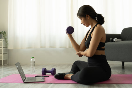 Young asian woman doing fitness exercises at home through virtual classの写真素材
