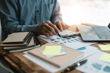 Close up of businessman or accountant hand holding pen working on calculator to calculate business data, accountancy document and laptop computer at office, business conceptの写真素材