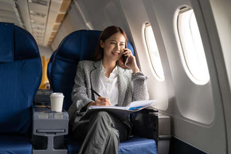 Young attractive and successful business asian woman talking on the phone and working while sitting in the chair of his private business planeの写真素材
