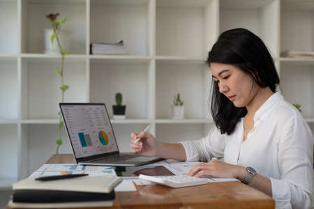Woman accountant working on laptop computer with financial document, graph diagram and calculator on...