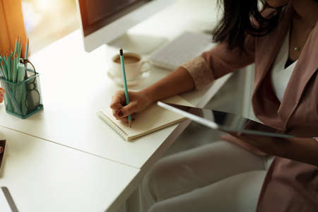 Cropped photo of woman writing making list taking notes in notepad working or learning on laptop indoors- educational course or training, seminar, education online conceptの写真素材