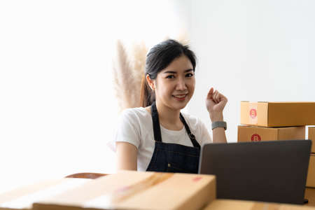 Portrait business owner smiling and feeling happy while preparing packages to ship to customers. Young woman with a lot of online ordersの写真素材
