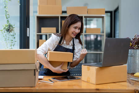 Happy business asian woman with parcel shipping box and exciting with new order. Entrepreneur small business working at home.の写真素材