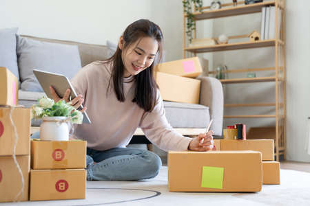 Female online store small business owner entrepreneur seller packing shipping ecommerce box checking website retail order using laptop preparing delivery parcel.の写真素材