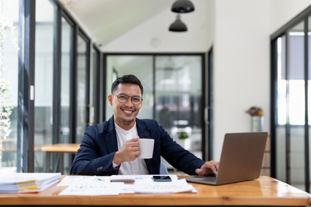 Portrait friendly smiling handsome asian businessman sitting and using laptop computer at office.の写真素材