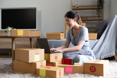 Start up small business, SME female owner checking order online to prepare to pack a box of goods for sale to customers, sme business idea.の写真素材