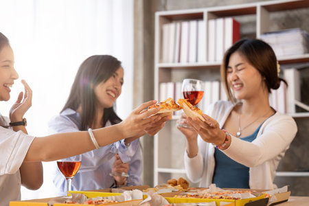 Group of Asian friends gather to celebrate Christmas with champagne and eating pizza at home. Joy of...