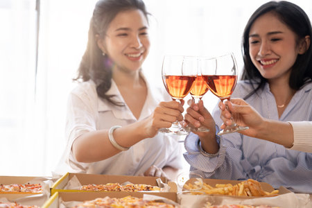 Group of Asian friends gather to celebrate Christmas with champagne and eating pizza at home. Joy of...