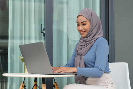 Portrait of Muslim asian woman in hijab using laptop at home.の写真素材