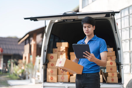 Asian courier with parcel and delivery logistic concept. Delivery man checking address order from cardboardの写真素材