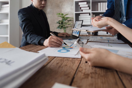 Business team using a calculator to calculate the numbers of statistic business profits growth rate on documents analyzing graph data, desk in the officeの写真素材