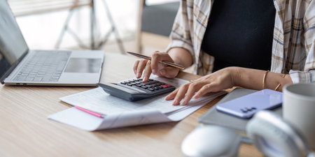 Young asian female work with financial papers at home count on calculator before paying taxes receipts online by phone. Millennial woman planning budget glad to find chance for economy saving moneyの写真素材