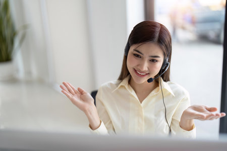 Portrait of happy smiling female customer support phone operator at workplace. Smiling beautiful Asian woman working in call centerの写真素材