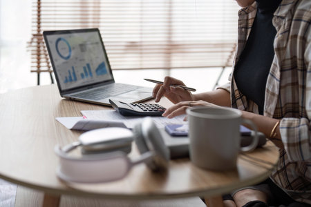 Young asian female work with financial papers at home count on calculator before paying taxes receipts online by phone. Millennial woman planning budget glad to find chance for economy saving moneyの写真素材