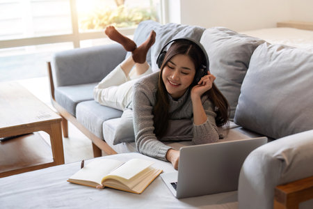 Young woman lying on sofa and listening to music relaxing with eyes closedの写真素材