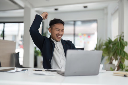 Happy young businessman looking at laptop excited by good news online, lucky successful winner man...