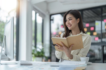 Young Asian businesswoman sitting at their desk and take notes using laptop in the officeの写真素材