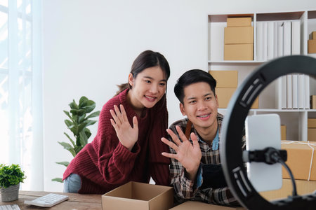 young couple mobile phone recording live streaming in online social media selling products by couple, doing freelance, own business or entrepreneur at home. E-commerce, shopping conceptの写真素材