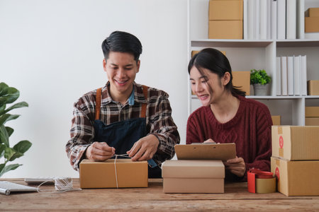 startup small business owner working with computer at workplace. freelance man and woman seller check product order, packing goods for delivery to customer. Online selling, e-commerceの写真素材