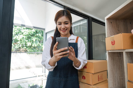 Young Asian online business owner using her smartphone to gather more information sell product on line shop while sitting in her roomの写真素材