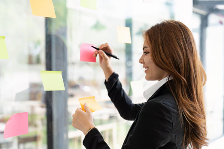 Asian businesswoman creating project plan on office wall with paper notes. Financial and Marketing projectsの写真素材